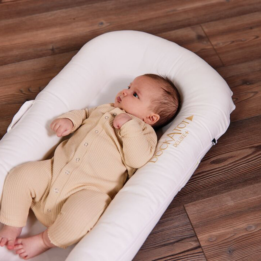 赤ちゃんがDockATot(プリスティンホワイト)で眠っている様子|木目フロア背景