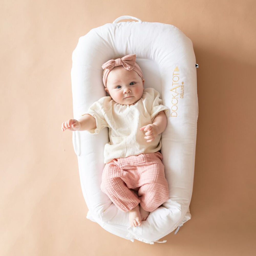 DockATot(プリスティンホワイト)で赤ちゃんがリラックスしている様子(ピンク背景)