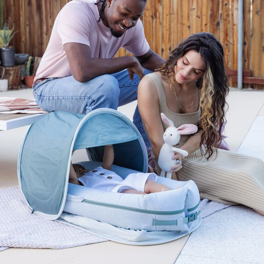 カバナキットをつけたDockATot（マリンシャンブレー）で屋外でママとパパと遊ぶスキンシップシーン